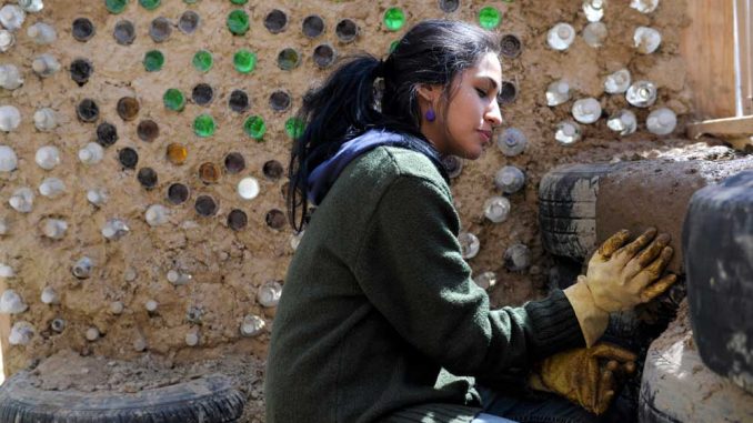 Lu Thain smooths a clay mixture on a tire on the earthship-style greenhouse. | ABI REIMOLD / TTN