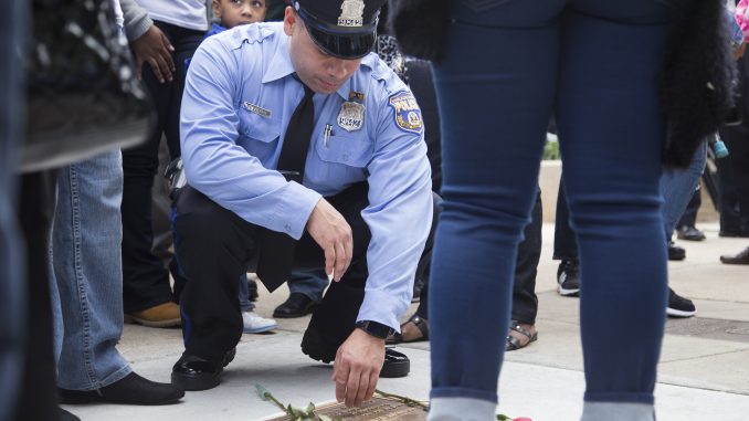 Officer Mike Rivera, who attended police academy with Robert Wilson III, leans over Wilson's plaque at Philadelphia Police's 22nd District Headquarters Wednesday. | Jenny Kerrigan TTN